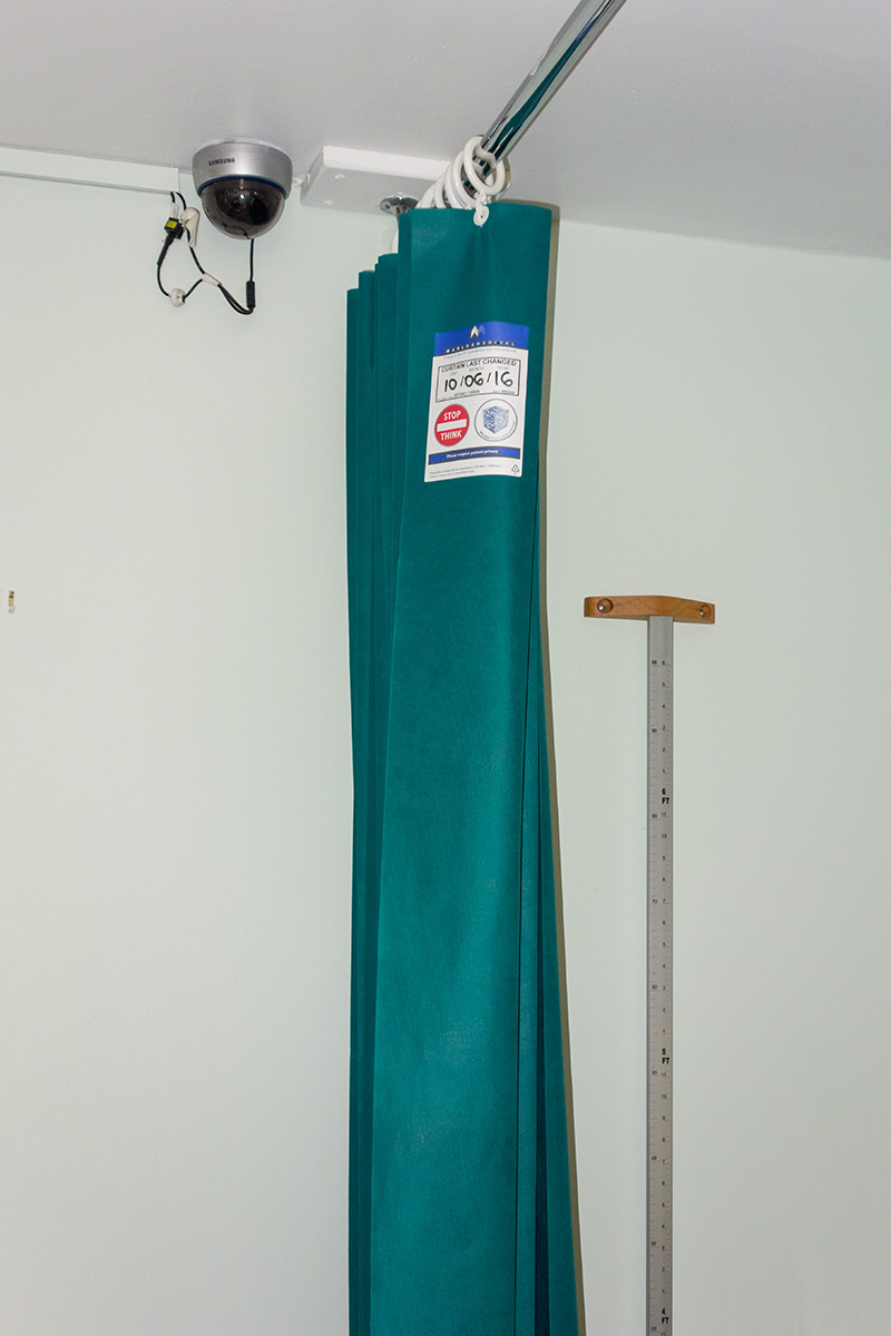 A domed security camera inside a clinic room at a health centre, positioned close to a privacy curtain