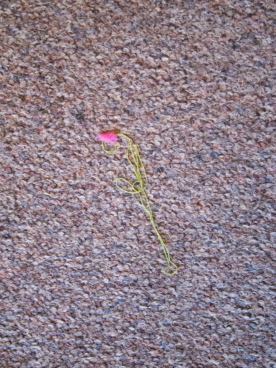 Green cotton and pink fluff with the appearance of a flower, on an office carpet
