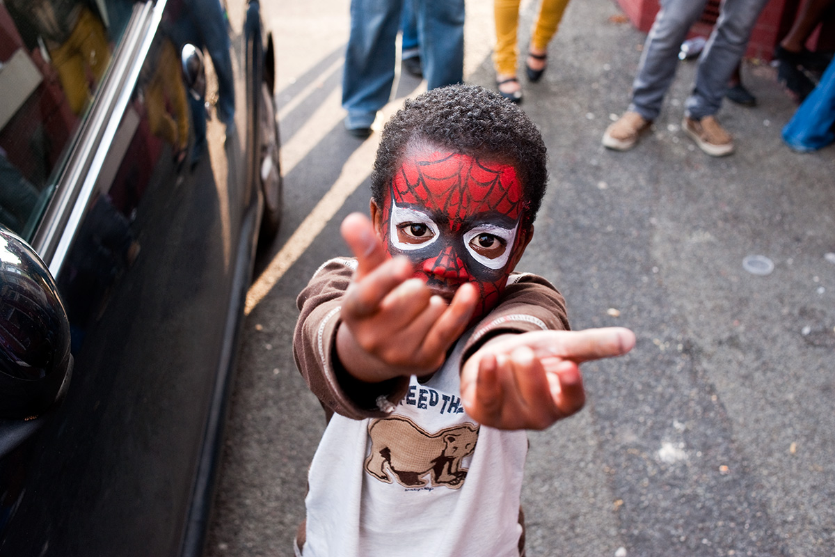 A boy wearing Spiderman face paint pretending to shoot web from his hands