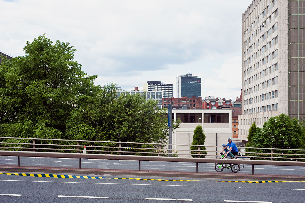 A father and son participating in the Great Manchester Cycle, riding along the Mancunian Way where it crosses Upper Brook Street