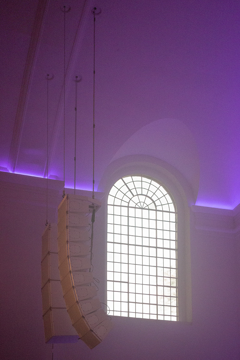 The curved ceiling of St John-at-Hackney Church, with suspended speakers and leaded window