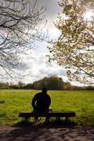 A man sitting on a bench, enjoying the view across a meadow area of Fletcher Moss, Didsbury, Manchester